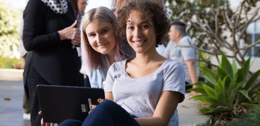 Two young women holding a tablet sitting outside